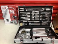 Closed aluminum carrying case filled with stainless steel BBQ tools and digital grill thermometer next to the case.