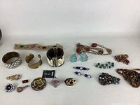 Wide assortment of vintage costume jewelry including bracelets, brooches, pins, earrings, and various beaded necklaces laid out on white surface.