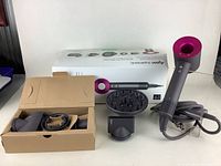 Overview of dryer, original box, brown tray holding three attachments, diffuser and styling nozzle on table