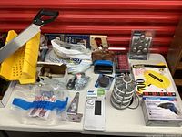 View of assorted tools and hardware on a table, including hacksaw, metal cage light, screws, and loose hardware in packaging.