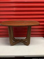 Front view of the mid-century modern wooden end table showing oval top and curved wooden base.