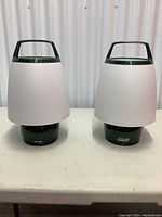 Two Coleman battery-operated lanterns side by side on a white table against a white backdrop.