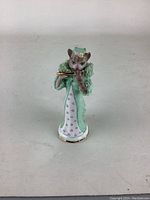 Front view of the cat figurine playing a flute, showing the lace and floral dress details.