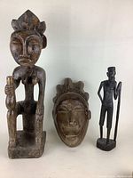 Photo showing all three wooden carvings together: tall seated female figure, mask, and standing male figure