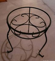 Photo of black wrought iron plant stand from side angle showing the scroll design and three curved legs.
