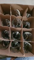 Top-down view of the 12 black wine glasses packed in a cardboard box with dividers, showing they are all intact and stored securely.