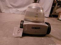 Front view of silver Conair steam iron with visible water tank showing water levels and brand name on base with wheels.