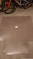 Large clear rubber desk mat with textured underside placed on a concrete floor near bicycles.