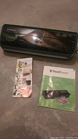 FoodSaver vacuum sealer with two manuals on concrete flooring, showing front detail and logos.