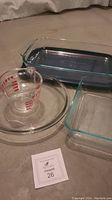 Four Pyrex glass baking items arranged on the floor including two rectangular baking dishes, one round bowl, and one glass measuring cup.