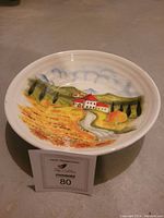 Large ceramic hand-painted bowl with sunflower landscape scene inside, showing red roof house, trees, path, and hills.
