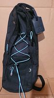 Full view of black oxygen tank backpack with blue elastic cords on the front and a black tag attached to the handle.