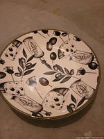Large round white ceramic plate with black illustrations of olives, cheese wedges, olive branches, and olive oil bottles.