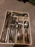 Photo showing full flatware set in a beige plastic organizer with multiple compartments including knives, forks, spoons, and smaller spoons.
