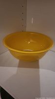 Front view of a small yellow glass bowl placed on a white surface inside a white cabinet, showing its shape and color.