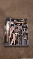 Top view photo of a gray plastic silverware organizer with various utensils and silverware inside.