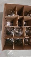 Top-down view of 9 clear wine glasses in a cardboard box with dividers.
