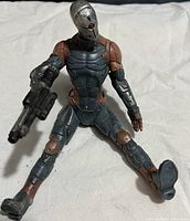 A seated cyborg action figure with silver and brown body armor holding a black futuristic gun, on a white background.