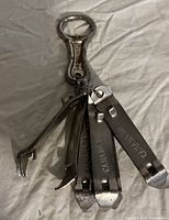 Three metal vintage bottle openers on gray background, including a ring style keyring opener with additional prying tools and two flat stamped openers.