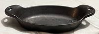Oval black cast iron baking dish with handles on each side, shown from top angle on white surface.