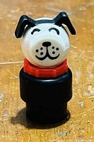 Single small plastic toy modeled as a white dog head with black ears and facial features, a red collar, and a black cylindrical body sitting upright.