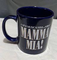 Front side of a blue mug showing promotional text for the Mamma Mia musical.