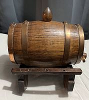 Miniature wooden whiskey barrel on a wooden stand, showing the full barrel with three metal hoops and a wooden stopper on top.