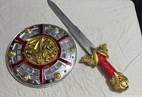 Photo showing plastic toy shield and toy sword on white fabric background.