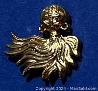 Front view of gold-tone metal pin shaped like a fleur-de-lis with detailed ridges and texture on a blue background.