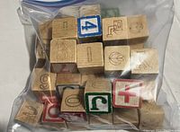 Plastic bag containing approximately 28 vintage wooden toy blocks with numbers, letters, and symbols printed on their sides in multiple colors.