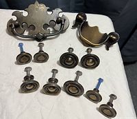 Photo showing eight vintage round drawer knobs and two brass drawer handles with attached screws arranged on a fabric surface.