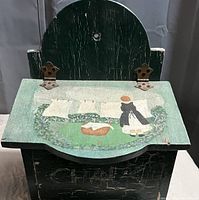 Front view of the vintage wooden wall mount storage box with a painted lid showing a girl hanging laundry outdoors. Hinges on the lid are visible.