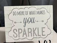 Photo shows the wall plaque with the quote 'Do more of what makes you sparkle' in decorative fonts with glitter details.
