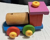 Side view of wooden toy train showing blue base, red and green wheels, purple and red blocks for cabin, and natural wood cylinder body.