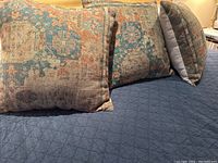 Three blue, rust, and beige printed euro pillow covers with antique rug pattern shown on dark blue quilt surface, arranged leaned against a sofa.