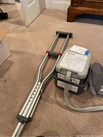 Aluminum crutches alongside Ossur Cold Rush Compact ice therapy unit; crutches have adjustable holes, rubber grips and tips; therapy unit has attached hose and cooling pad.