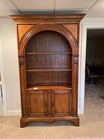 Front view of full bookcase cabinet showing arched top, two lower doors and interior shelf