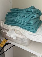 Stack of turquoise towels on top of white mattress pad and bed skirt, all items appear used and neatly folded, boxed for convenience.