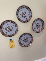 Overview of all four decorative plates arranged on a wall, showing each one with bird, fruit and floral motifs and brown floral border