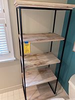 Full view of the shelving unit showing four wooden shelves supported by a black metal frame in a room corner.
