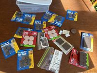 Photo showing an assortment of furniture pads in original packaging and loose pads on a table, along with a plastic container.