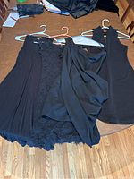 Four black dresses laid out on a wood table showing different textures, fabrics and styles: sleeveless maxi, lace off-shoulder, body-con knit, and one-shoulder draped dress.