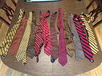 Twelve vintage men's silk ties laid out on wooden table, showing various patterns and colors