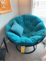 Full view of papasan chair with teal cushion and matching throw pillow set in a corner near window blinds.