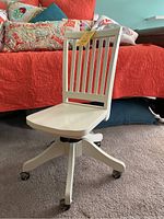 View of off white Pottery Barn Kids adjustable swivel desk chair on carpet with slatted backrest and caster wheels.
