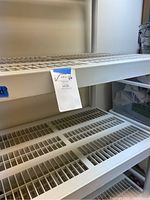 Close-up of white Rubbermaid style plastic shelf with grid pattern and label indicating lot number 66.