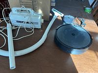 Oreck handheld vacuum in white with hose and attachments laid out on a table in natural light.