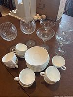 Full lot showing white Wedgwood teacups, plates, margarita glasses, and etched red wine glasses arranged on a table.