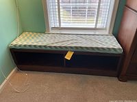 Full view of the brown wood bench with chevron cushion against a windowed wall.