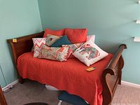 Wood twin sleigh style bed showing the full side view with orange bedspread and pillows on it.